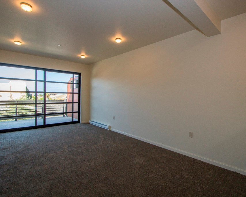 an empty living room with a large window and carpeted flooring